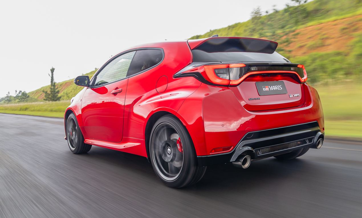 Toyota GR Yaris vermelho em movimento visto pela traseira, destacando lanternas em LED interligadas, aerofólio esportivo, difusor traseiro e escapamento duplo cromado.