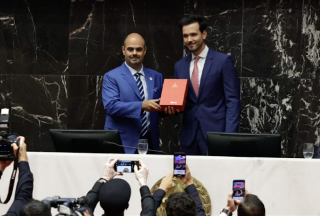 Governador Mateus Simões recebe documento oficial durante cerimônia de posse na Assembleia Legislativa de Minas Gerais, com presença de autoridades e imprensa