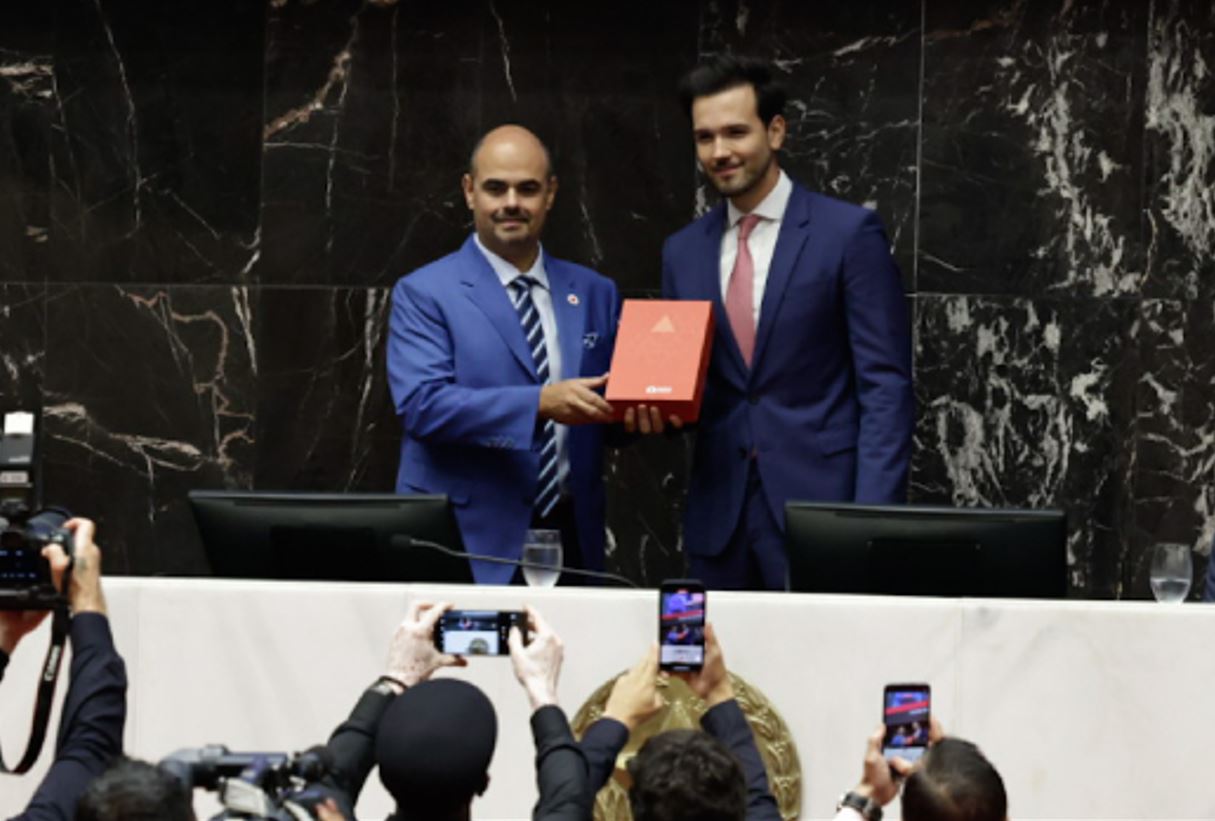 Governador Mateus Simões recebe documento oficial durante cerimônia de posse na Assembleia Legislativa de Minas Gerais, com presença de autoridades e imprensa