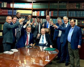 Juristas e autoridades brindam durante cerimônia de posse na Academia Nacional de Direito Desportivo, em sala com estantes repletas de livros jurídicos.
