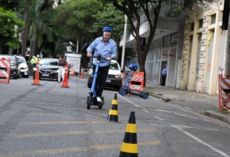 Homem utilizando patinete elétrico em via urbana de Belo Horizonte durante demonstração prática, com cones de sinalização e veículos ao fundo