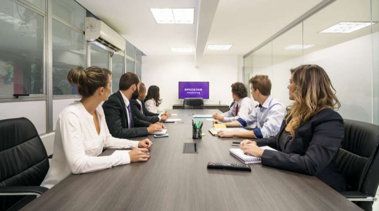 Profissionais reunidos em sala de reunião moderna do Spacejob Coworking, em Belo Horizonte, assistindo apresentação em ambiente corporativo colaborativo.