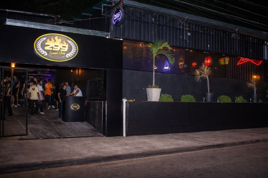 Fachada do 299 Speed Shop à noite em Belo Horizonte, com iluminação em neon, entrada movimentada e pessoas reunidas na porta.