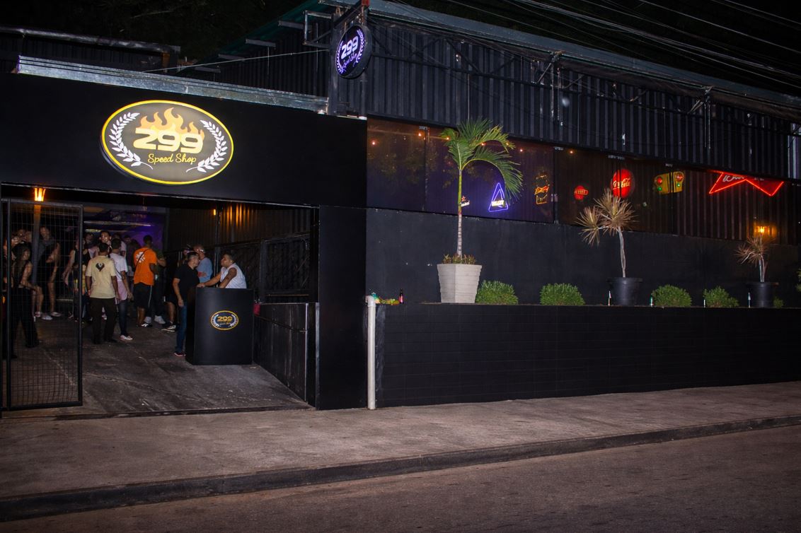 Fachada do 299 Speed Shop à noite em Belo Horizonte, com iluminação em neon, entrada movimentada e pessoas reunidas na porta.