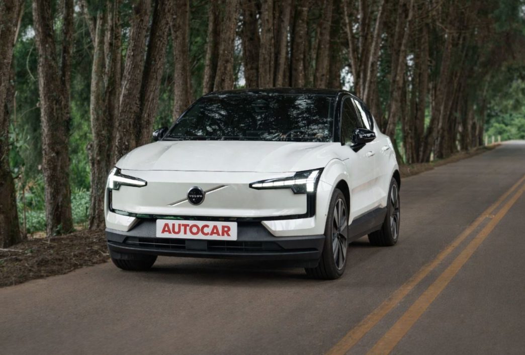Volvo EX30 Ultra Twin Motor elétrico em movimento em estrada cercada por vegetação, destacando design moderno e iluminação frontal característica da marca.