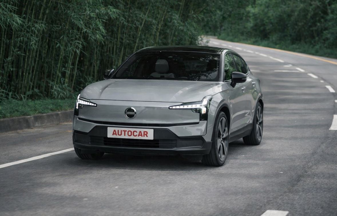 Volvo EX30 Ultra Twin Motor elétrico em movimento em estrada cercada por vegetação, destacando design moderno e iluminação frontal característica da marca.