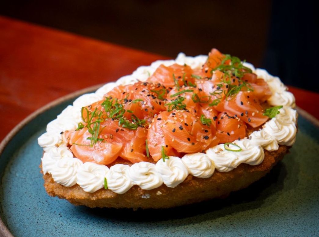 Ovo de sushi crocante servido em prato, coberto com fatias generosas de salmão fresco, cream cheese, gergelim e cebolinha.