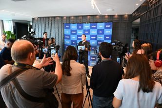 Presidente da FIEMG concede entrevista coletiva, cercado por jornalistas e câmeras, diante de painel institucional da entidade.