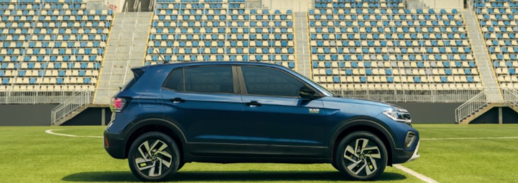 Volkswagen T-Cross Seleção azul em vista lateral, estacionado em campo de futebol com arquibancadas ao fundo