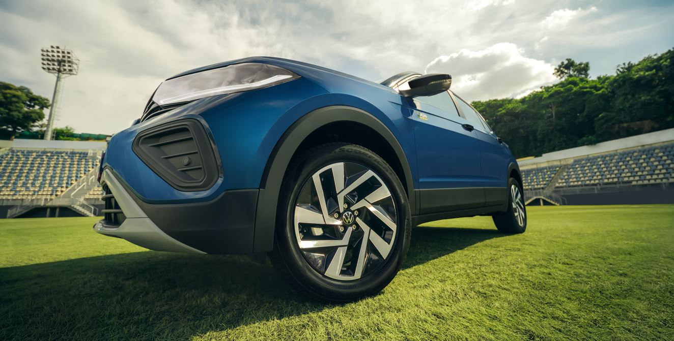 Detalhe da roda e lateral do Volkswagen T-Cross Seleção azul em campo de futebol, com design esportivo e rodas de liga leve