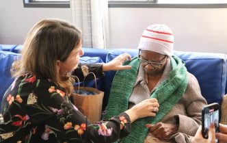 Mulher entrega cachecol verde a idoso durante ação solidária da campanha Calor Humano do Servas em Belo Horizonte.