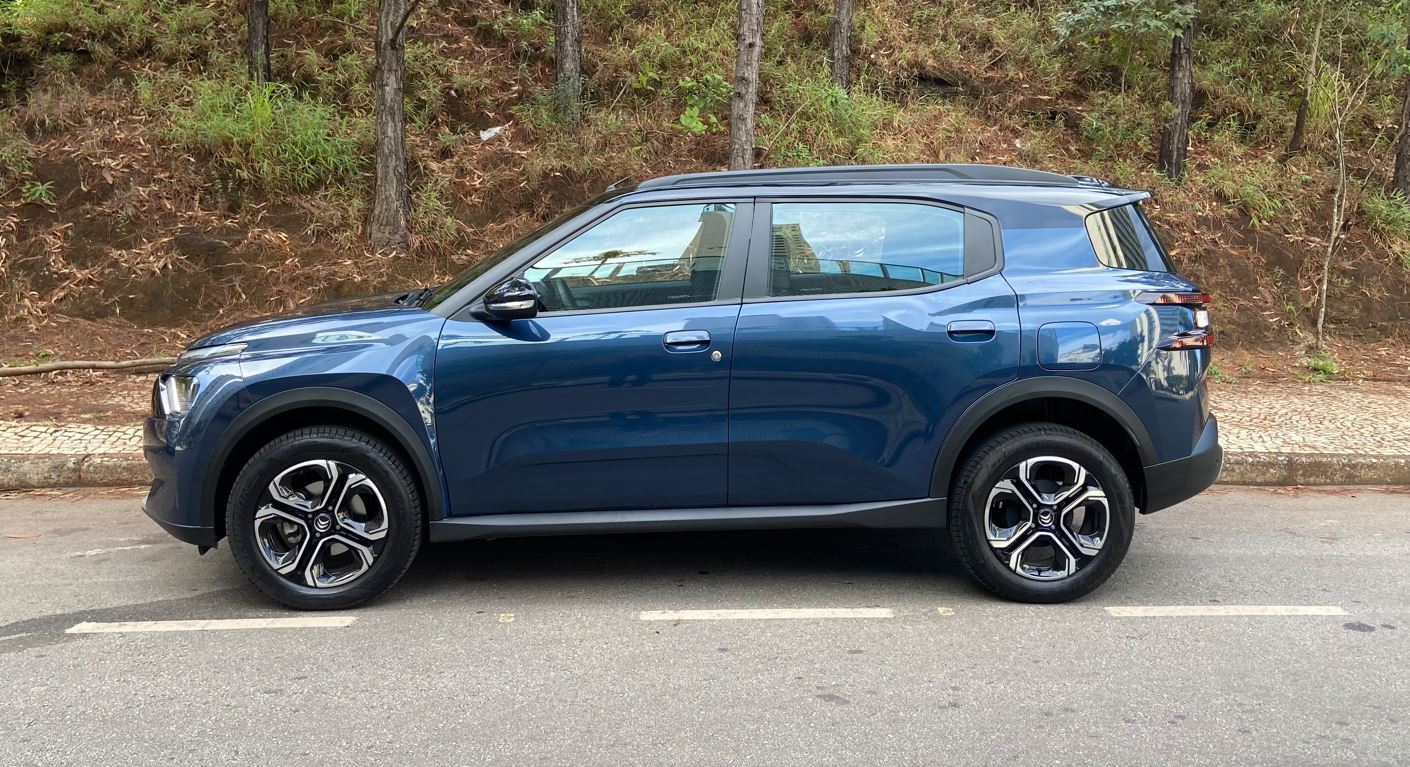 Citroën Aircross XTR 7 2026 azul visto de perfil, estacionado em via urbana, destacando carroceria alongada, rodas de liga leve, barras de teto e proposta familiar de sete lugares.