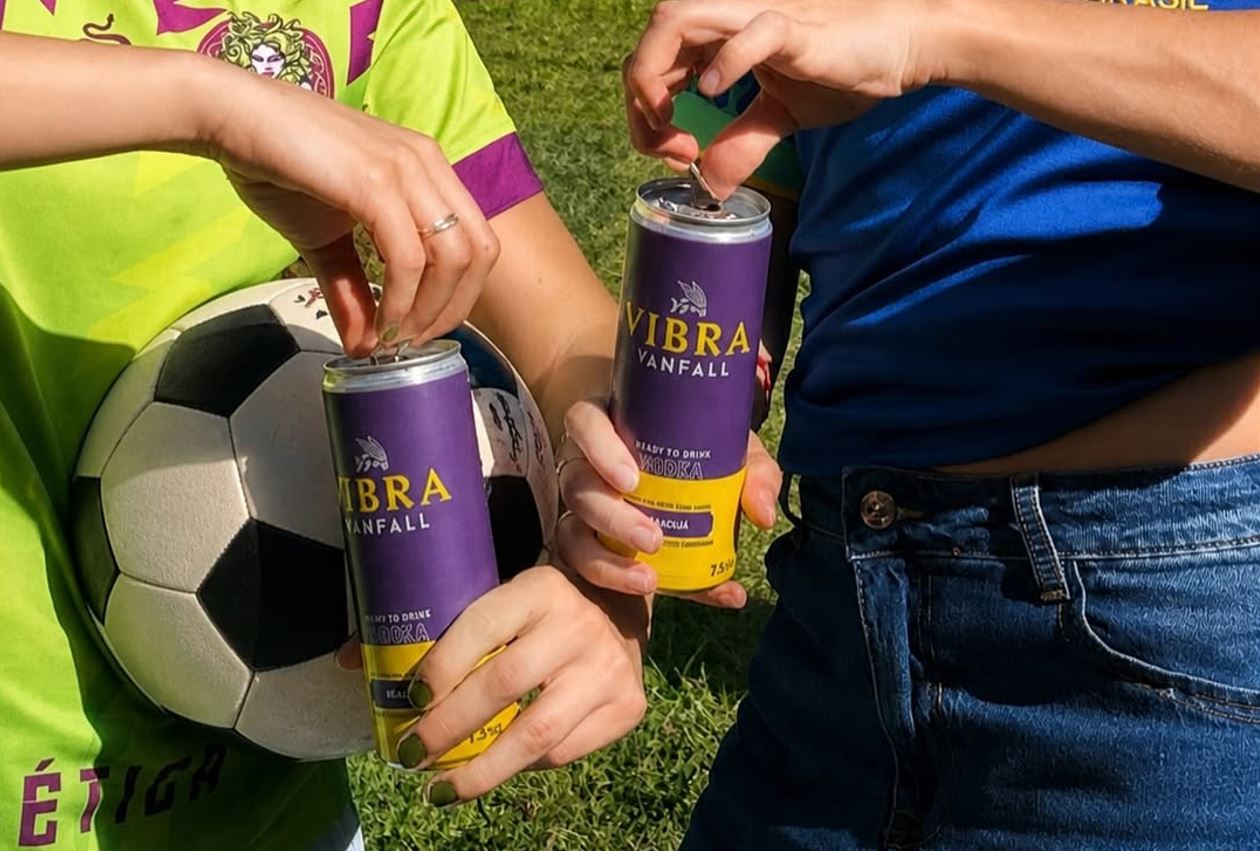 Chope e drinks grátis embalam gols do Brasil na Copa 3 Duas pessoas seguram latas de drink Vibra, da Vanfall, ao lado de uma bola de futebol, em clima de torcida pela Copa.