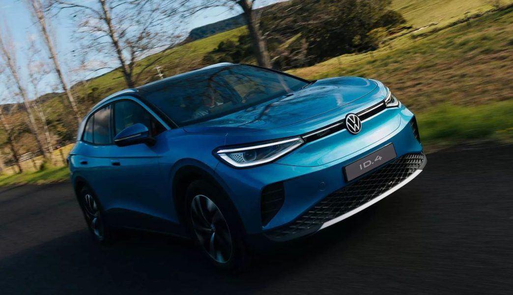 Volkswagen ID.4 azul em movimento por uma estrada rural, visto de frente, com destaque para os faróis, logotipo VW e linhas aerodinâmicas do SUV elétrico.