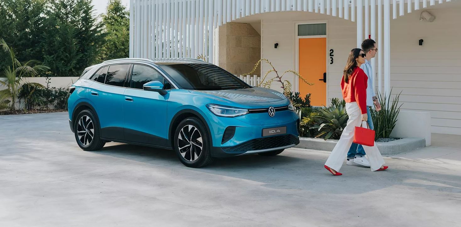 Volkswagen ID.4 azul estacionado em frente a uma residência moderna, com duas pessoas caminhando ao lado do SUV elétrico.
