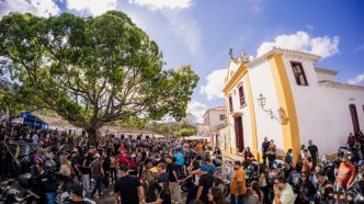 Multidão participa do Bike Fest Tiradentes no centro histórico da cidade, com motocicletas, visitantes e igreja colonial ao fundo.