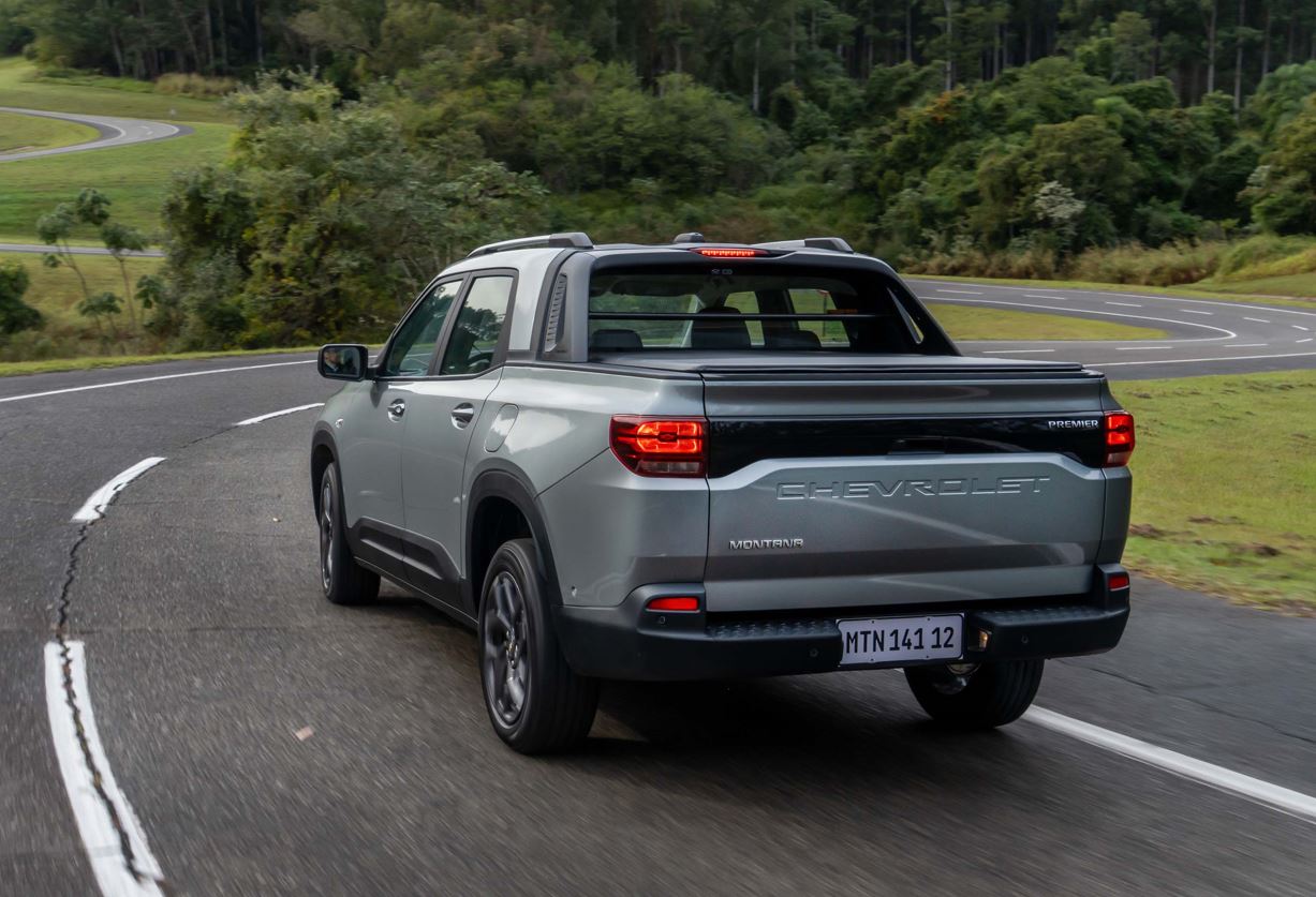 Chevrolet Montana 2027 cinza em movimento na estrada, vista pela traseira, destacando caçamba, lanternas, Santo Antônio integrado e tampa com nome Chevrolet.