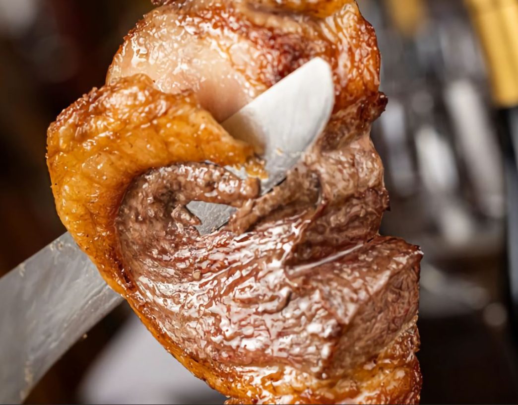 Close de uma peça de carne assada sendo fatiada no espeto durante o rodízio da churrascaria Porcão BH, em Belo Horizonte.