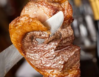 Close de uma peça de carne assada sendo fatiada no espeto durante o rodízio da churrascaria Porcão BH, em Belo Horizonte.