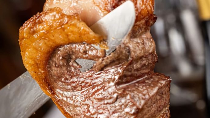 Close de uma peça de carne assada sendo fatiada no espeto durante o rodízio da churrascaria Porcão BH, em Belo Horizonte.