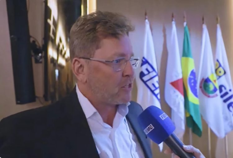 Guilherme Abrantes concede entrevista diante das bandeiras da FIEMG, de Minas Gerais e do Brasil, após a eleição para a presidência da entidade.