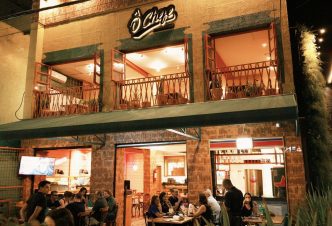 Fachada iluminada do Ô Chefe Steakhouse em Belo Horizonte, com clientes sentados nas mesas externas durante a noite.