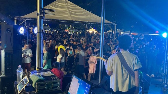 Vista do palco durante apresentação de rock, com músico de costas tocando guitarra diante de um grande público reunido em evento noturno.