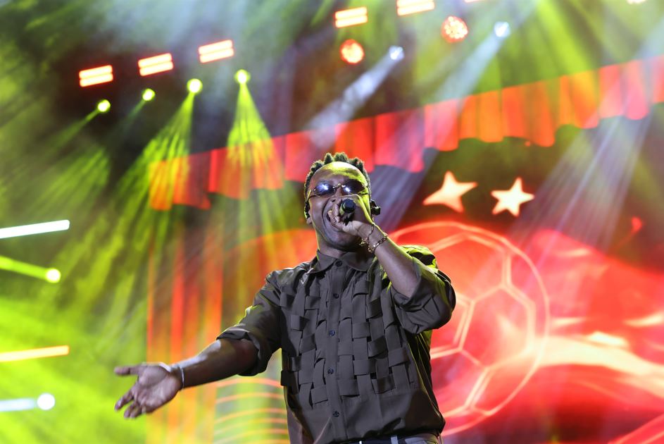 Thiaguinho canta ao microfone durante apresentação com iluminação verde e vermelha no Fiat Festival 50 anos.