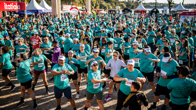 Grande grupo de corredores com camisetas azul-turquesa participa de atividade coletiva em arena da Corrida Itatiaia, em Belo Horizonte, com estruturas do evento ao fundo.