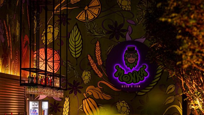 Interior da Monka Cervejaria, com balcão, torneiras de chope e mural colorido com lúpulo, frutas e logotipo.