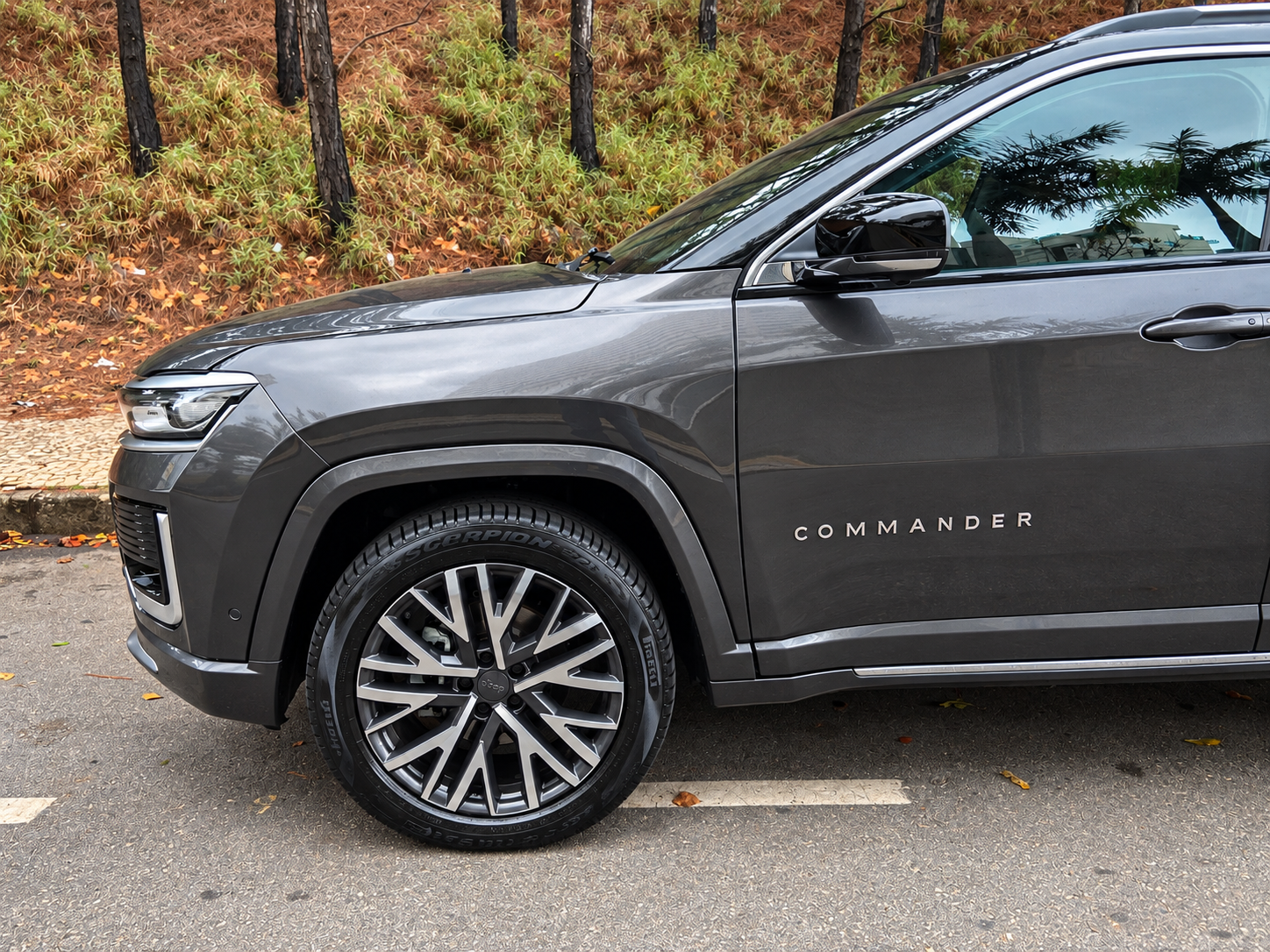 Detalhe lateral do Jeep Commander 2027 com roda de liga leve, pneu Pirelli Scorpion, para-lama robusto e identificação Commander na porta.