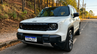 Jeep Renegade Sahara MHEV branco visto de frente e de lado, estacionado em uma via arborizada, com grade de sete fendas, faróis redondos e rodas de liga leve.