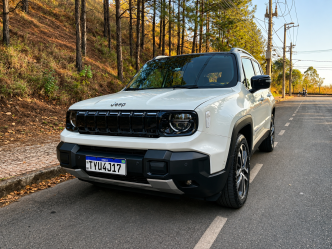 Jeep Renegade Sahara MHEV branco visto de frente e de lado, estacionado em uma via arborizada, com grade de sete fendas, faróis redondos e rodas de liga leve.