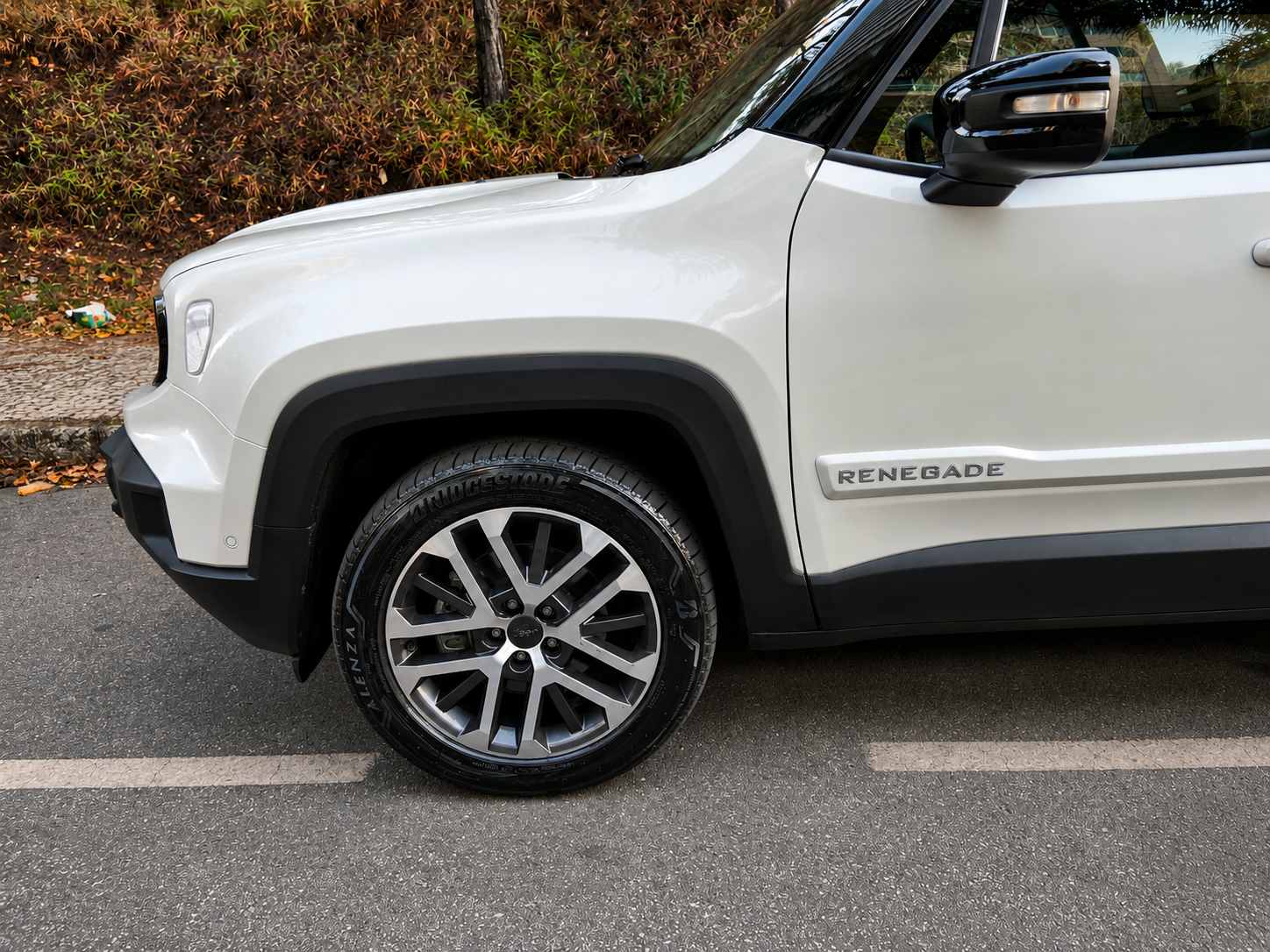 Detalhe da roda dianteira do Jeep Renegade Sahara MHEV branco, com roda de liga leve de 18 polegadas, moldura preta no para-lama e identificação Renegade na lateral.