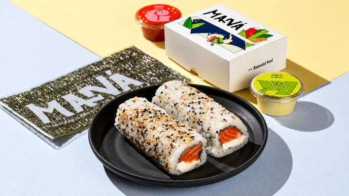 Hand rolls de salmão com cream cheese e gergelim em prato preto, acompanhados de nori e embalagens do Maná Hand Roll.