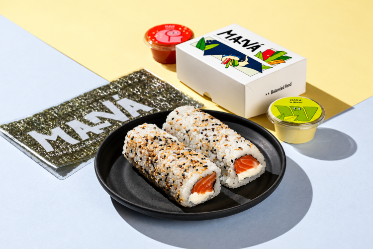 Hand rolls de salmão com cream cheese e gergelim em prato preto, acompanhados de nori e embalagens do Maná Hand Roll.