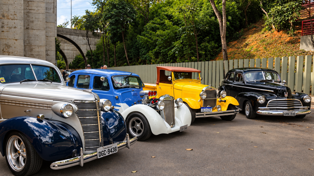 Carros antigos e hot rods coloridos reunidos em exposição automotiva, com modelos clássicos em destaque.