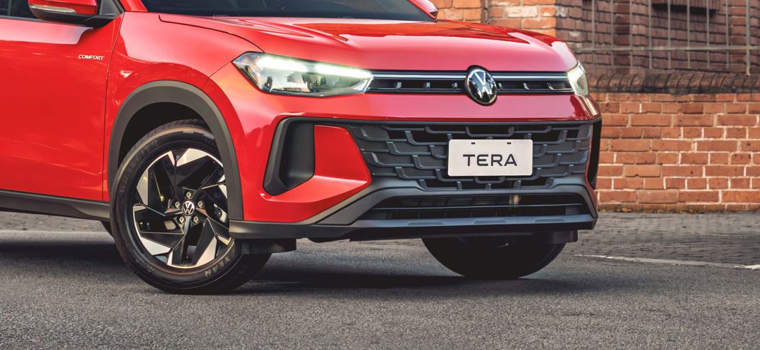 Detalhe frontal do Volkswagen Tera vermelho, com faróis de LED acesos, grade preta, para-choque robusto e roda de liga leve.