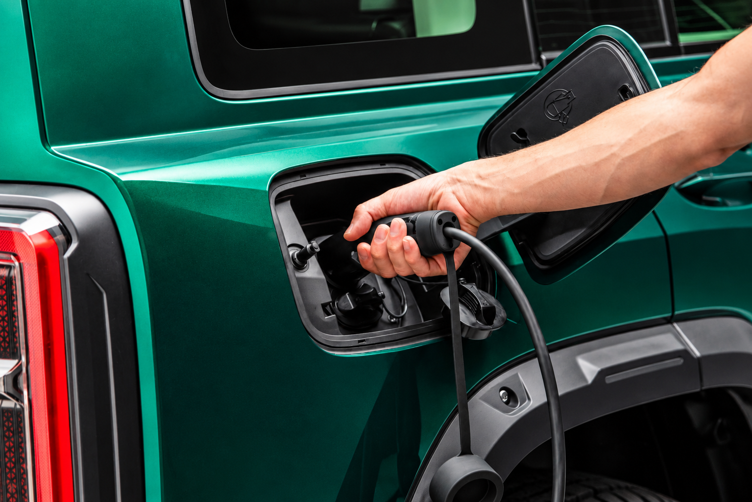 Detalhe da entrada de recarga elétrica do GWM Haval H7 híbrido plug-in flex na cor Verde Tijuca, com tampa aberta e pessoa conectando o cabo de carregamento à carroceria do SUV.