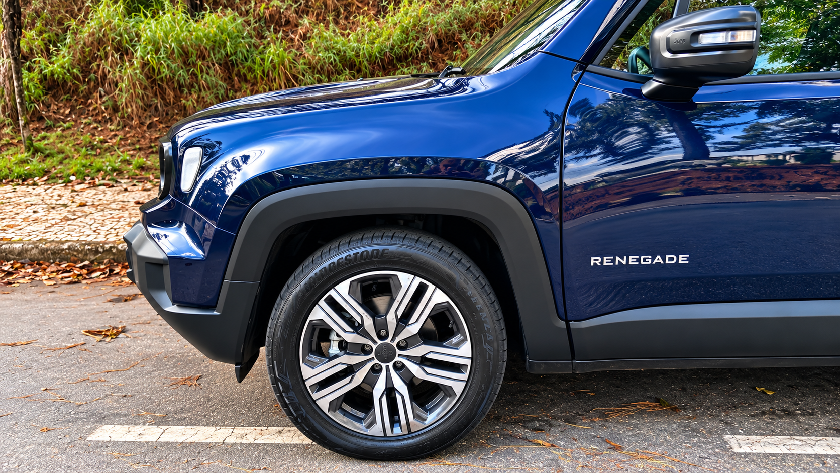 Detalhe lateral do novo Jeep Renegade Longitude MHEV azul, destacando roda de liga leve de 18 polegadas, pneu Bridgestone, caixa de roda trapezoidal e retrovisor com seta integrada.
