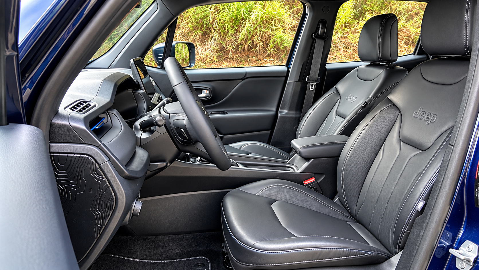 Interior do novo Jeep Renegade Longitude MHEV, com bancos dianteiros em revestimento preto, costuras aparentes, logotipo Jeep e console central renovado.